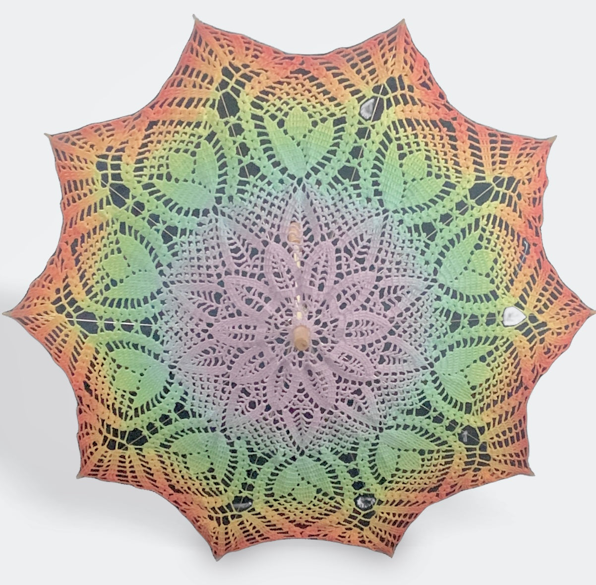 A parasol is open and facing the viewer. This is a self-drafted pattern and features the ROYGBIV rainbow for gaypride with pastel purple at the center and red at the edge.