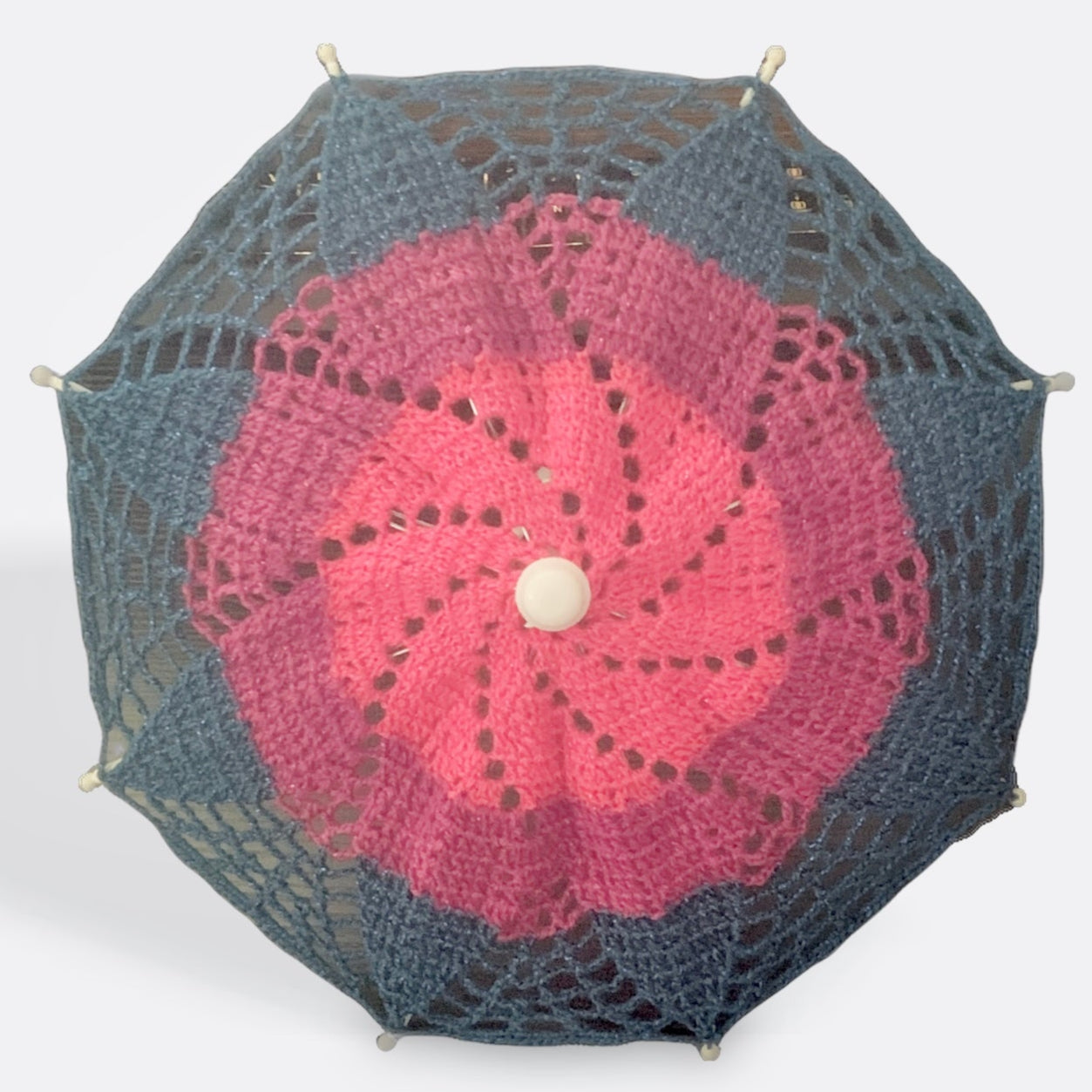A 12" parasol is open and facing the camera. Its crochet mandala features the Bisexual Pride flag with pink at the center, light purple in the middle, and blue at the edge.