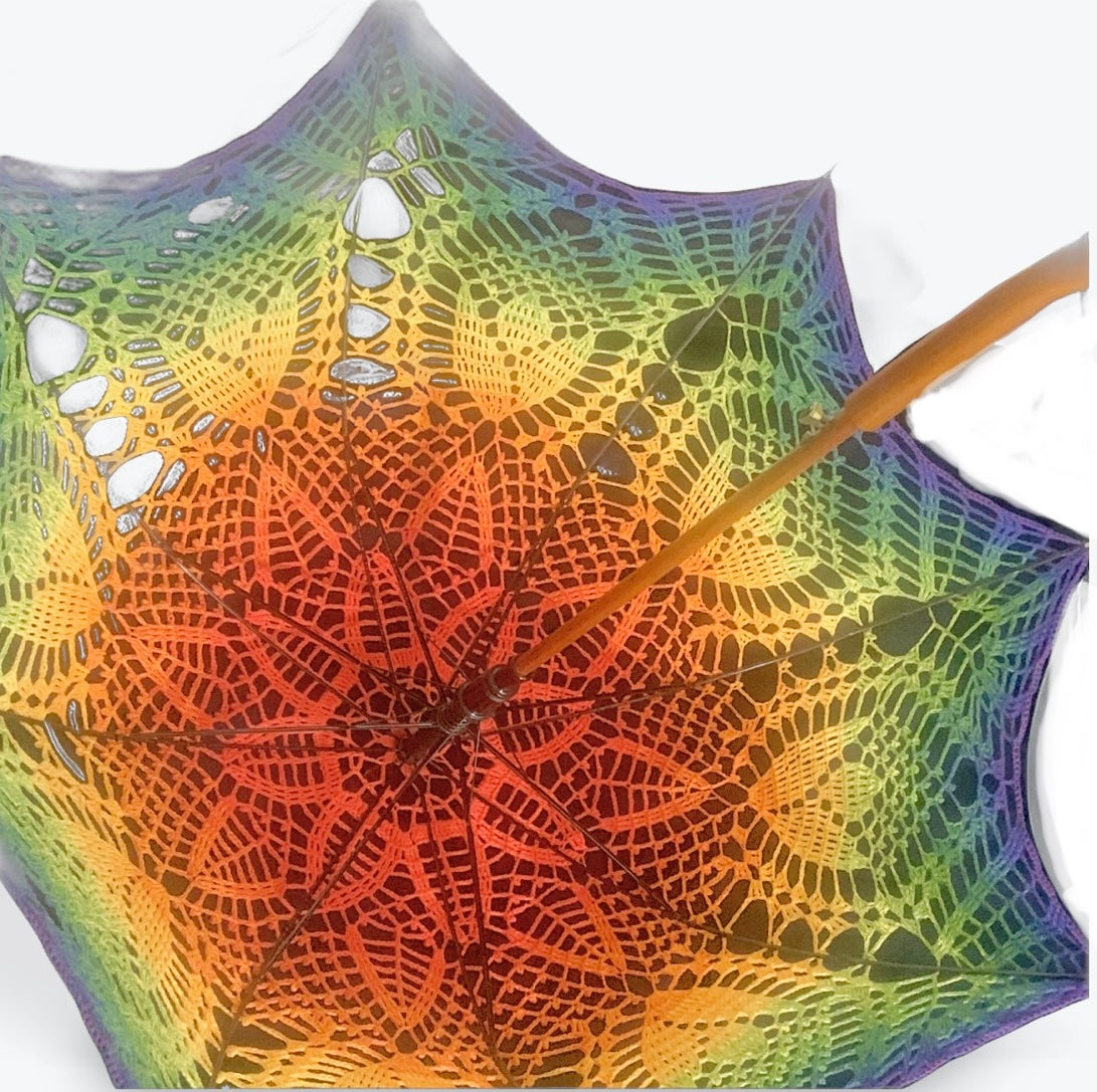 A 48" parasol is open and viewed from beneath as though you were holding it over your head. The wood handle and shaft are visible as well as the self-drafted pattern beginning with red at the center and fading gradually through the rainbow until it's purple at the edge.