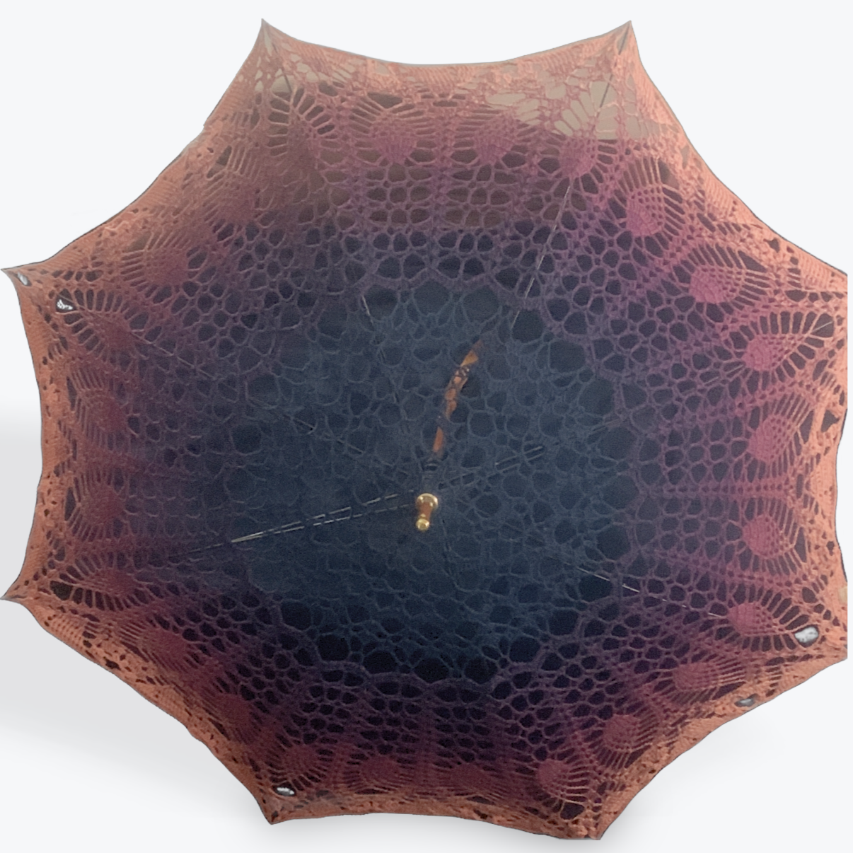 A parasol is open and facing the viewer. At the center a brass top stands out against navy blue intricate pattern which fades into mauve and then peach at the edge. This pic was taken only in sun light.