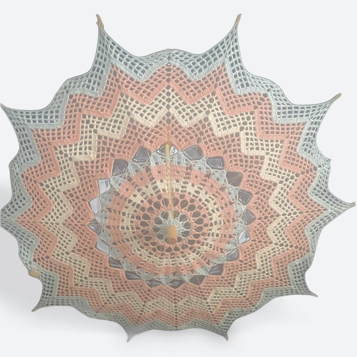 A parasol is open and facing the viewer. A very light wood decorative topper is visible at the center followed by concentric chevron shapes in blue, pink, white, pink, and blue for the transgender pride flag.