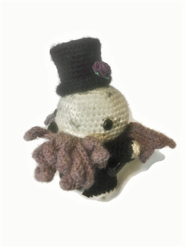 Dapper Cthulhu or Victorian Cthulhu has a black top hat, purple rose, greyish purple tentacles and wings, and is wearing a black suit. Made by Stitchy Frood. 