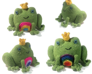 A green crochet frog with large eyes, large back legs, and small front legs appears with a gay pride flag circle on its belly, a small black smile, large blue eyes, and a golden crown sitting askew on its head is pictured in an endless white background.