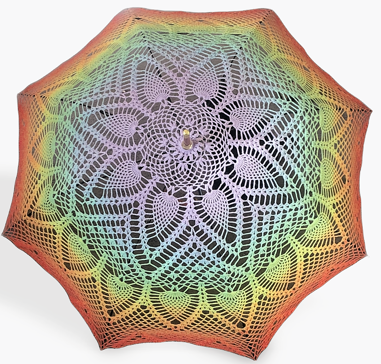A crochet mandala is attached to an umbrella frame and wide open. The mandala features the gay pride flag in a ROYGBIV rainbow from purple at the center to red at the edge. This umbrella is 48" wide when open. 