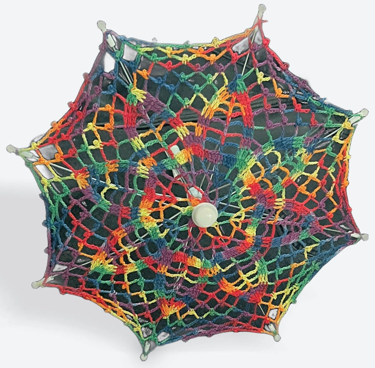 A 12" parasol is open and facing the camera. The canopy is crochet in rainbow variegated yarn and there are lots of rainbows packed in to this daisy pattern. This image has a dark background.