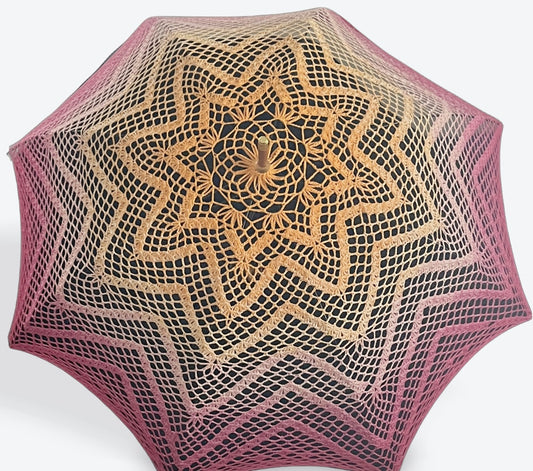 A parasol is open and facing the viewer tilted toward the top of the image. This parasol's cover is hand crocheted in a 100% cotton yarn features the colors of the Lesbian Pride flag. The pattern is 6 repeating concentric 8-pointed stars. 