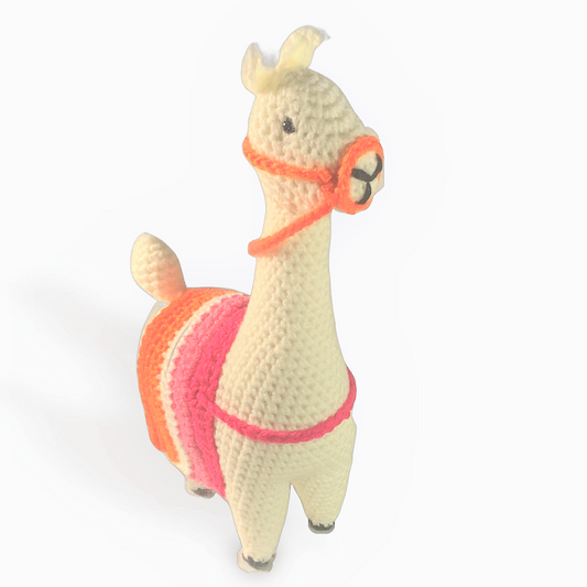 A off-white crocheted llama with a Lesbian Pride Flag striped blanket (dark pink, light pink, white, light orange, dark orange). The blanket is held on by a pink strap across the llama's chest. The llama is wearing an orange bridle and reins. The llama has black hooves, a black nose, and black eyes. The llama is standing on a white background.