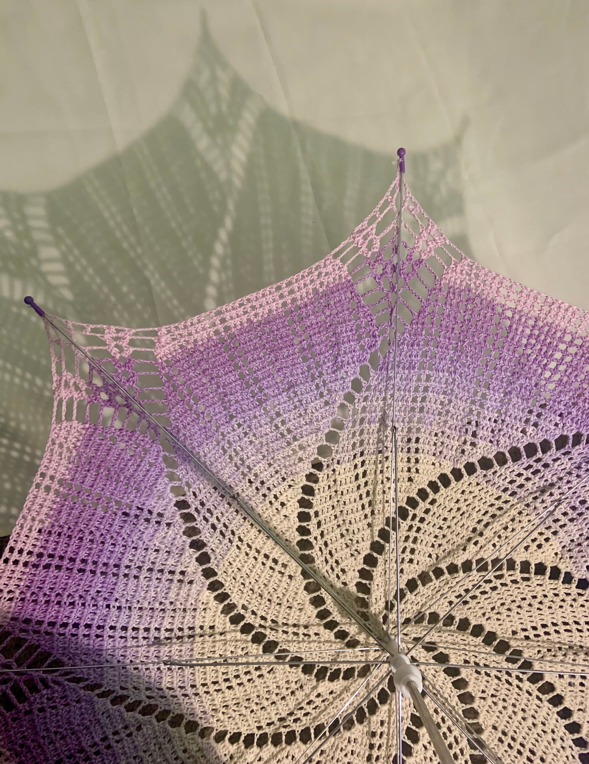 This picture shows part of a 30" parasol in cream, lavender, purple, and pink held upside down to show its very shady shadow behind. 