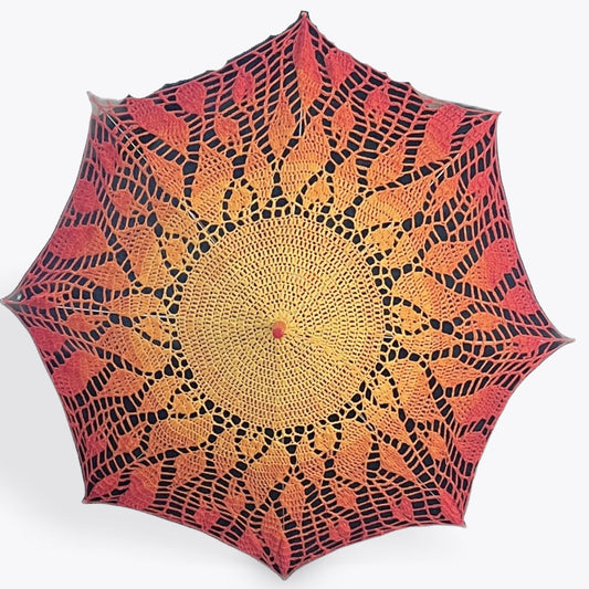 A parasol is open and facing the viewer. This parasol has a crochet doily for a dover which features an image of the sun, solid yellow at the center surrounded by small flame motifs fading through orange and red.  The parasol's plastic topper is red and found at the center of the yellow circle. It also has red details at the end of each of the 8 arms. 